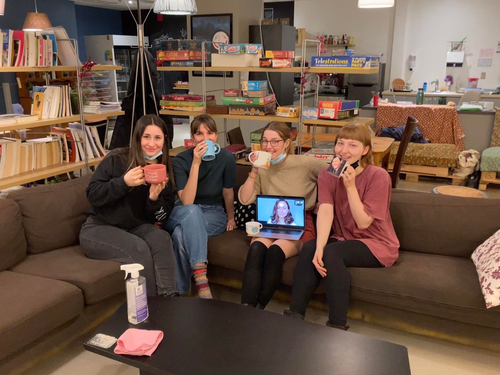 L'image montre les 5 employées du Philanthrope à l'hiver 2022. Elles sont assises sur le sectionnel du café, et tiennent ludiquement de jolies tasses disponibles au café.